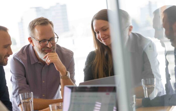 Alle zusammen sitzen am Tisch und schauen auf den Laptop.