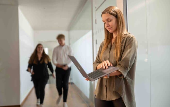 Alena schaut auf den Laptop, während Sandro und Pascale im Gang laufen.